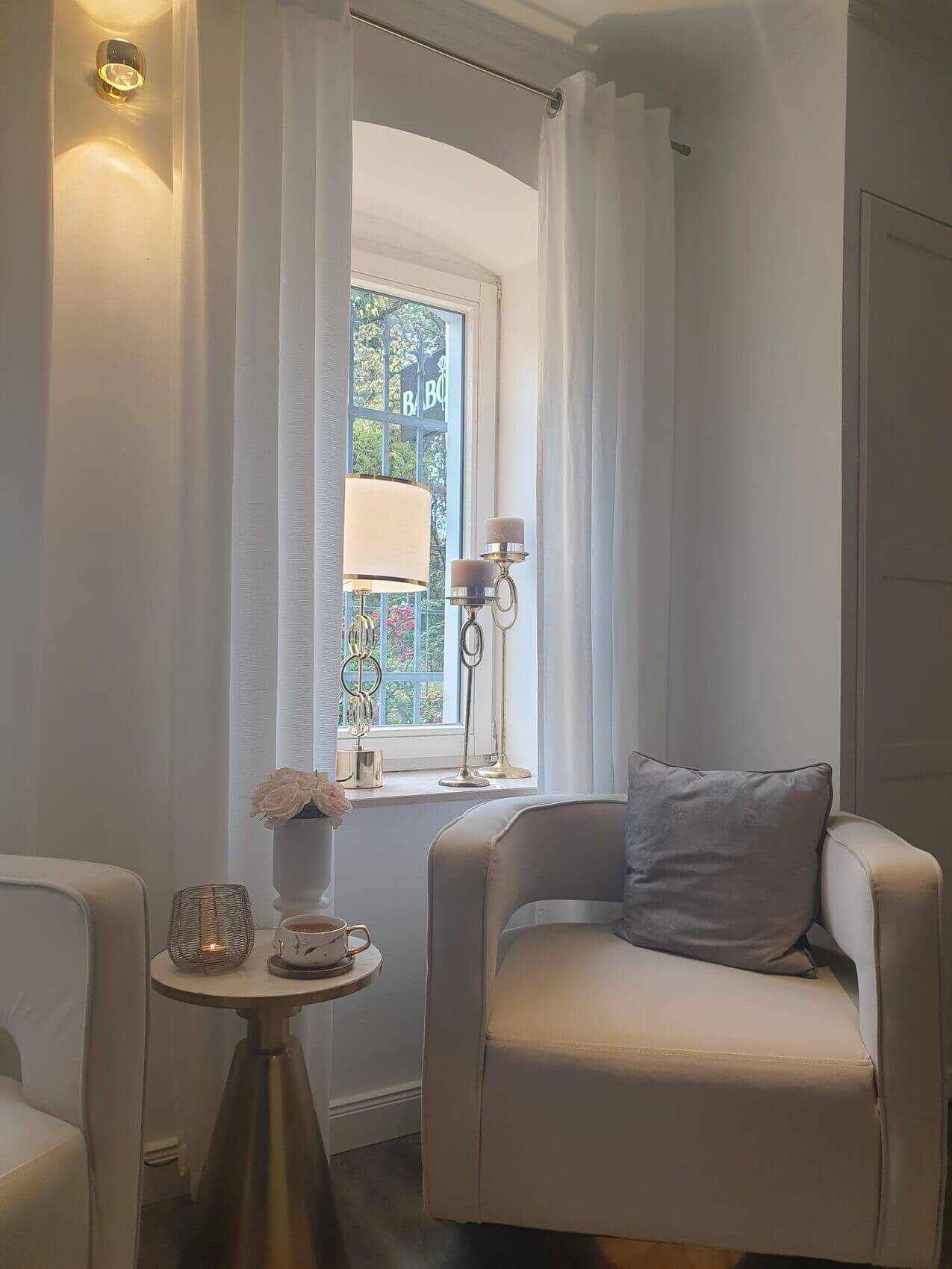 Ein elegantes Kosmetikstudio mit gemütlichem Sessel, Tisch mit Kerze und Tasse, verleiht eine entspannende Atmosphäre.