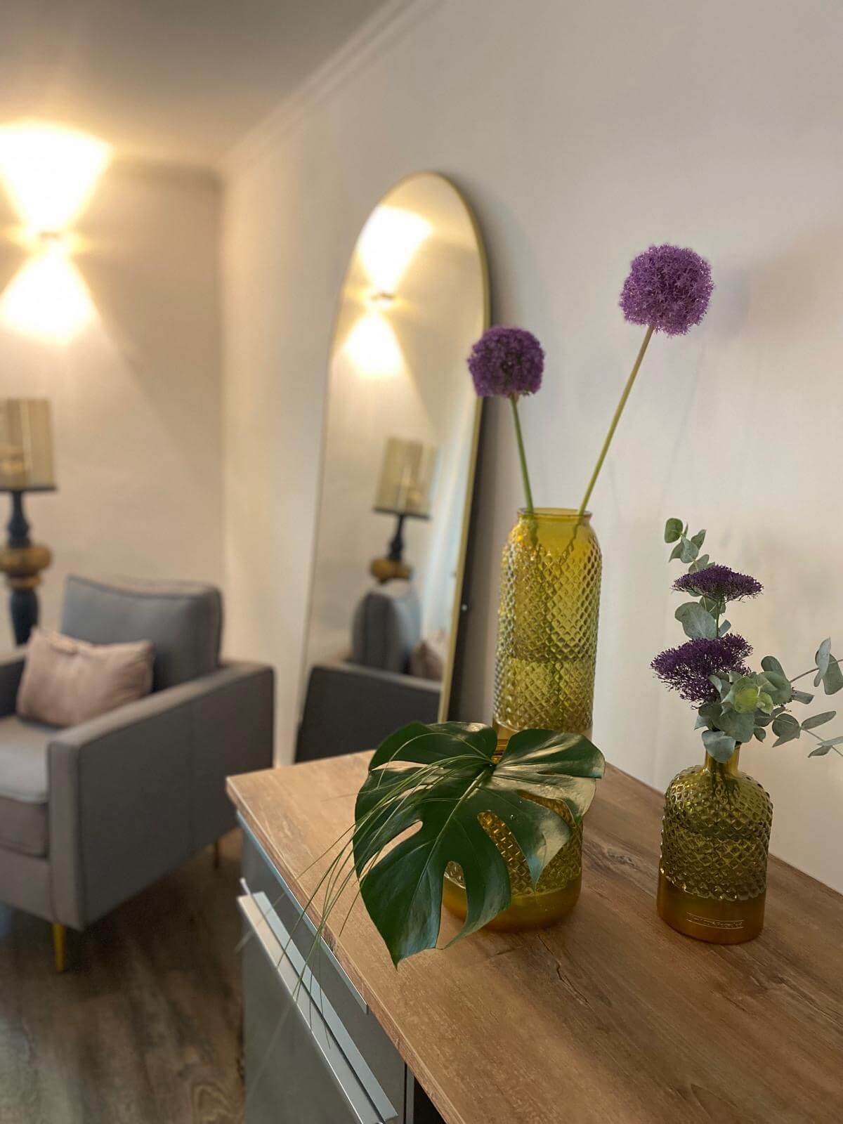Im Kosmetikstudio steht stilvoller Blumenschmuck in gelben Vasen neben einem Spiegel und einem gemütlichen Sessel.