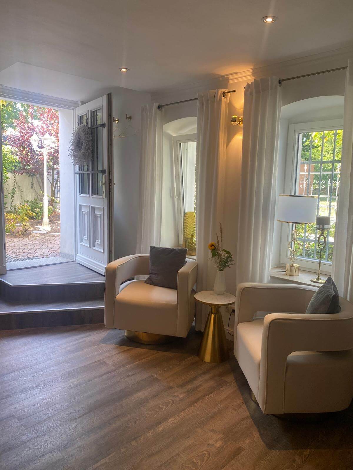 Gemütlicher Wartebereich in einem Kosmetikstudio mit zwei bequemen Sesseln und einem Blick nach draußen auf den Garten.