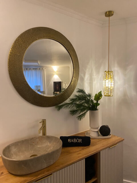 Ein stilvolles Kosmetikstudio mit einem goldenen Spiegel, luxuriösem Waschbecken und Babor-Handtuch auf der Holzkonsole.