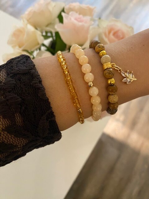 Ein Arm mit eleganten Armbändern wird vor einem Hintergrund mit rosa Rosen in einem stilvollen Kosmetikstudio präsentiert.
