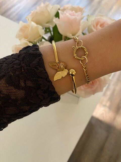 Eine elegant geschmückte Hand mit goldenen Armbändern und Rosen im Hintergrund vermittelt ein luxuriöses Kosmetikstudio-Ambiente.