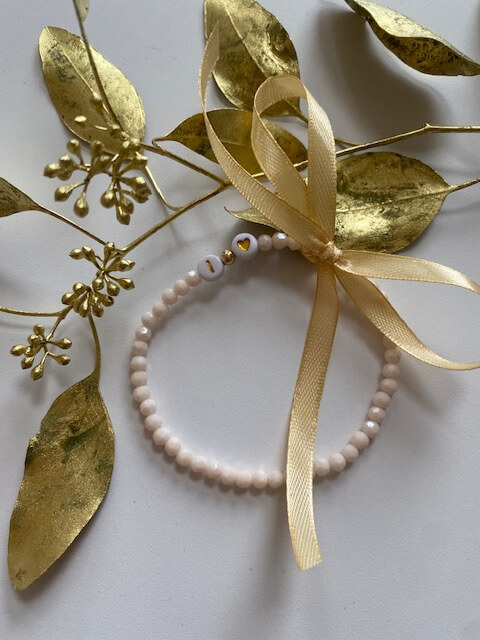 Ein zartes Perlenarmband mit goldenem Herzanhänger liegt dekorativ neben goldenen Blättern, ideal für ein Kosmetikstudio.